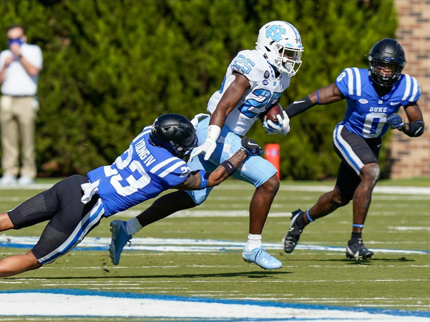 UNC running back Javonte Williams (25) runs for yardage tackled by Duke safety Lummie Young IV (23) and safety Marquis Waters (0) during the first quarter at Wallace Wade Stadium. Photo courtesy of Jim Dedmon-USA TODAY Sports