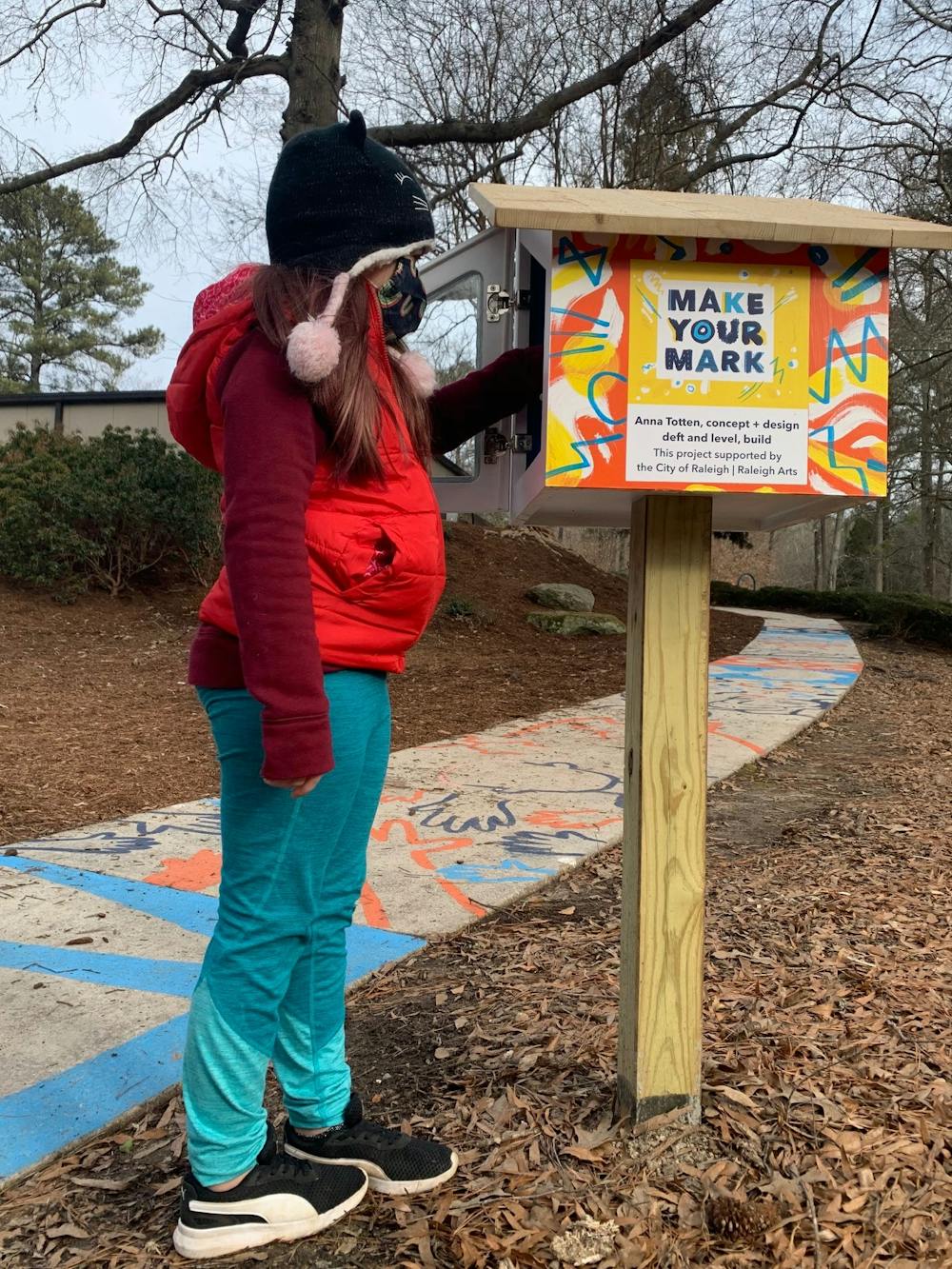A young girl stands by an interactive mural that is part of the Make Your Mark series of sidewalk murals around Raleigh. Photo courtesy of Anna Totten