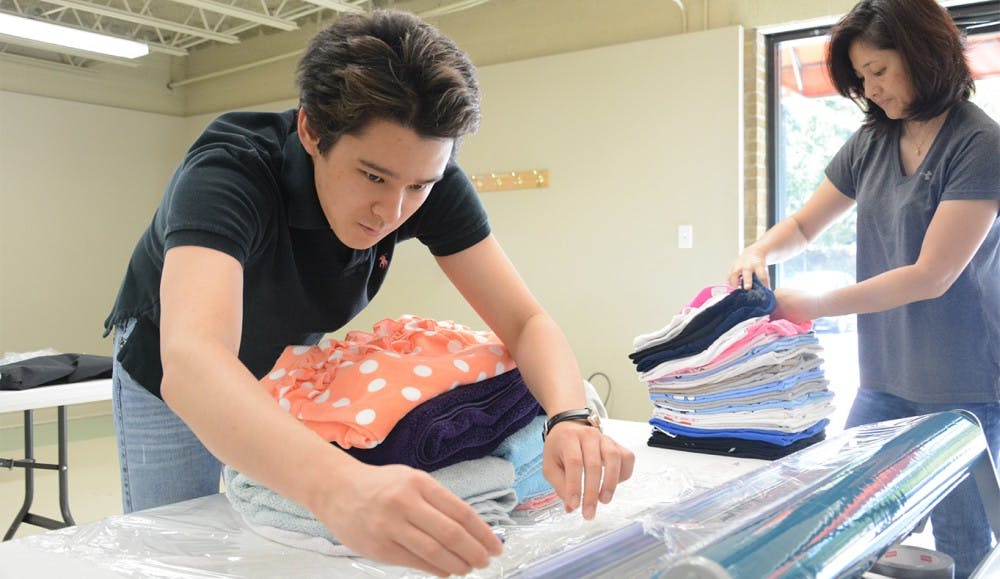 Shuya Osada works on getting folded clothes wrapped in plastic wrap while Yoshia Osada lends a hand.