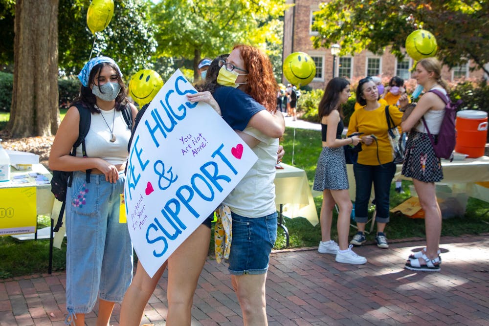 <p>Emily Midea, the mother of a first-year student, offers hugs to students behind the Old Well on Thursday. Parents and puppies filled the upper quad to offer hugs, baked goods and support as part of a parent rally organized by the Facebook group UNC-CH Parents Helping Parents.&nbsp;</p>