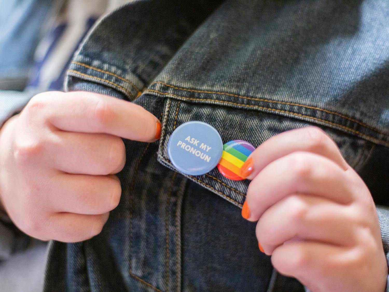 DTH Photo Illustration. A student shows off the "Ask my pronoun" and pride flag buttons pinned to their jacket.