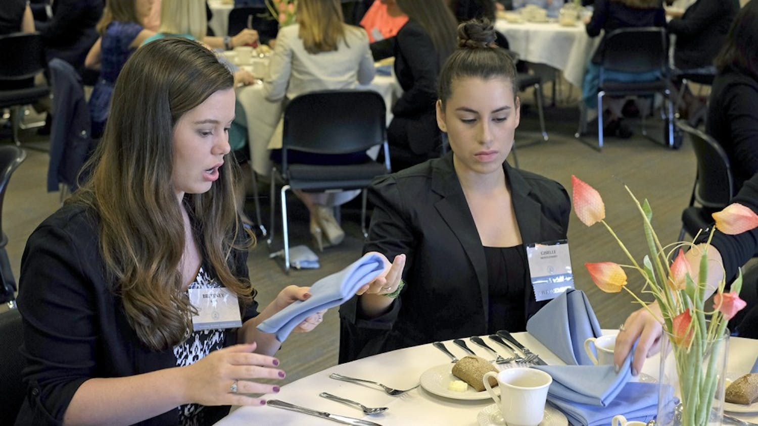 Brittney King and Giselle Montgomery attempt to set their silverware as a part of the etiquette dinner Tuesday evening.