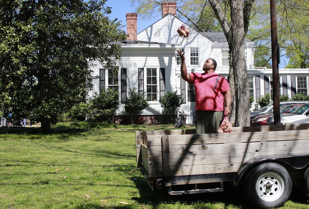 Jason Brown, a former UNC football player, tosses a sack of sweet potatoes into the air behind the UNC Study Center on Saturday. Brown, who left the NFL to become a farmer, donated 20,000 pounds of sweet potatoes to food banks and church programs across North Carolina. The potatoes were bagged up by local volunteers to be shipped out on Saturday. 