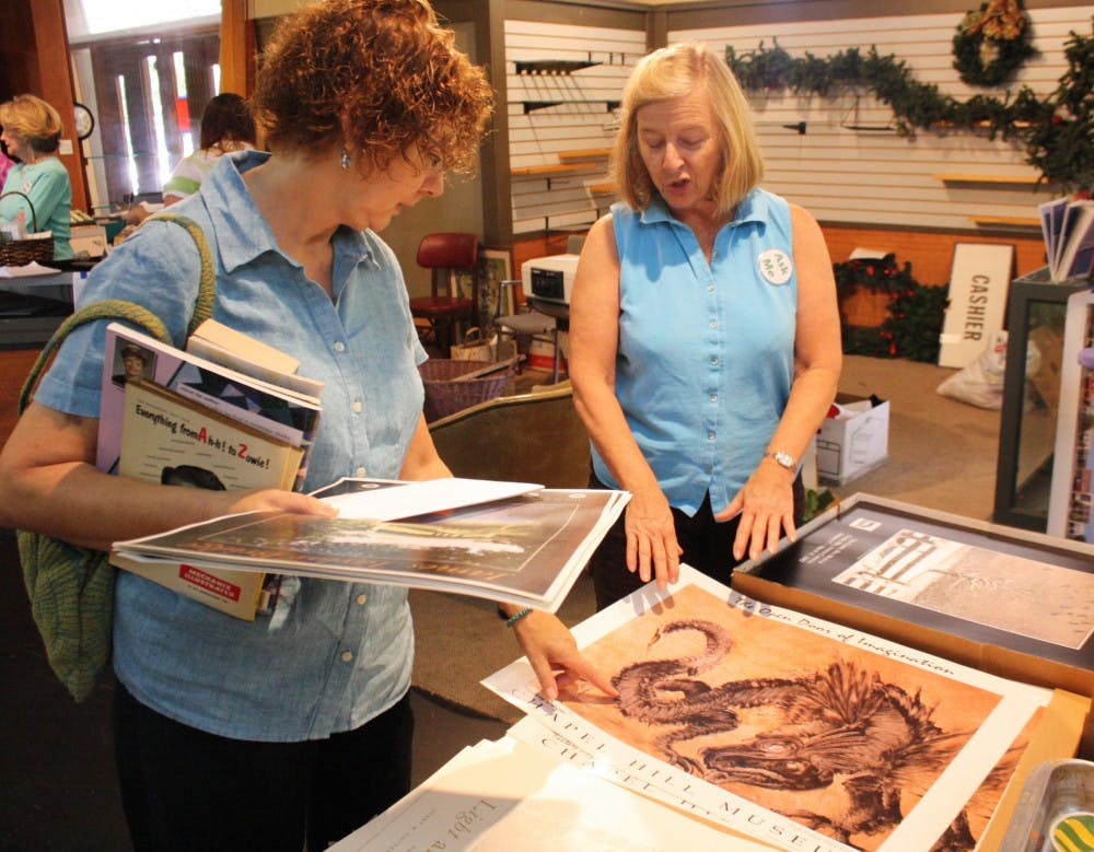 Jane Cousins (left) looks through posters at the Chapel Hill Museum yard sale Saturday with the help of a museum worker, UNC alumna Beth Isenhour.  The museum, located on Franklin Street is closing due to funding problems and is selling its old exhibits and memorabilia.  