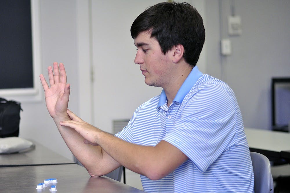 Jeff Powell, a senior biomedical engineering major and design chair of the UNC-Chapel Hill Biomedical Engineering Club, made a prosthetic arm for 7-year-old Holden Mora with 3-D printing technology. Powell uses the three model fingers on the table to explain how each part of the hand is made. 