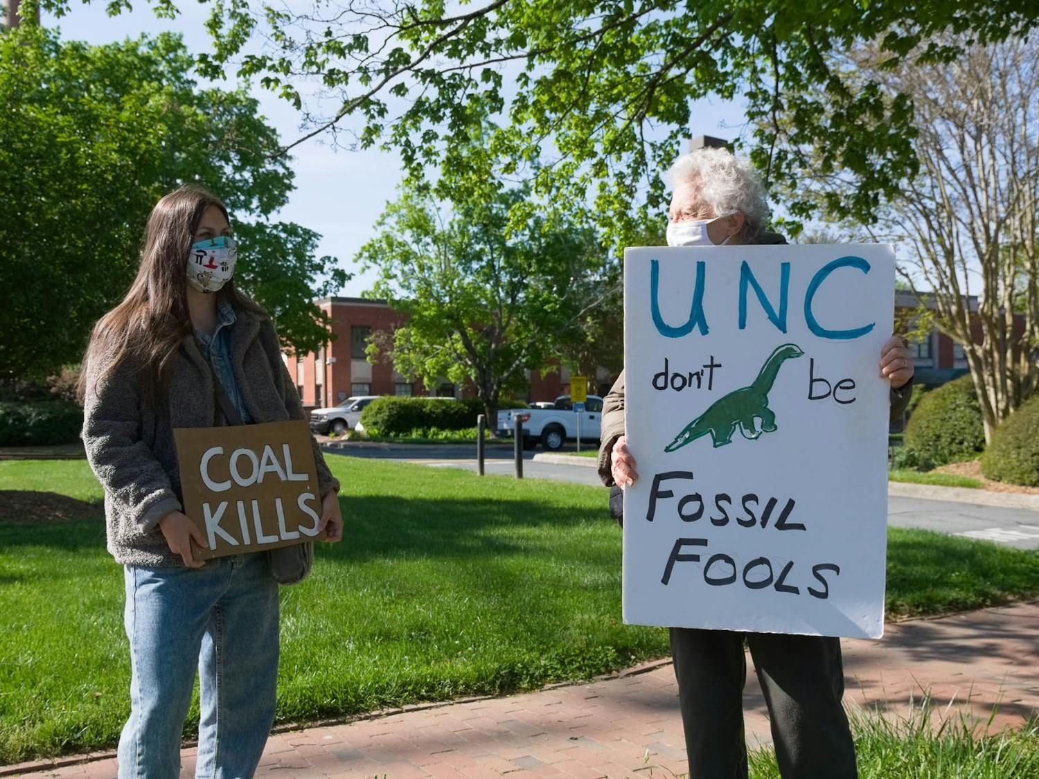 Amelia Covington and Judith Lechner hold up signs outside of UNC's coal plant on Friday, Apr. 23, 2021.