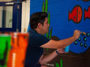 Antonio Alanís, the full-time artist at Frank Porter Graham Bilingüe Elementary, paints the "Mi Comunidad de FPGB" mural on Monday, Aug. 15, 2022.&nbsp;
