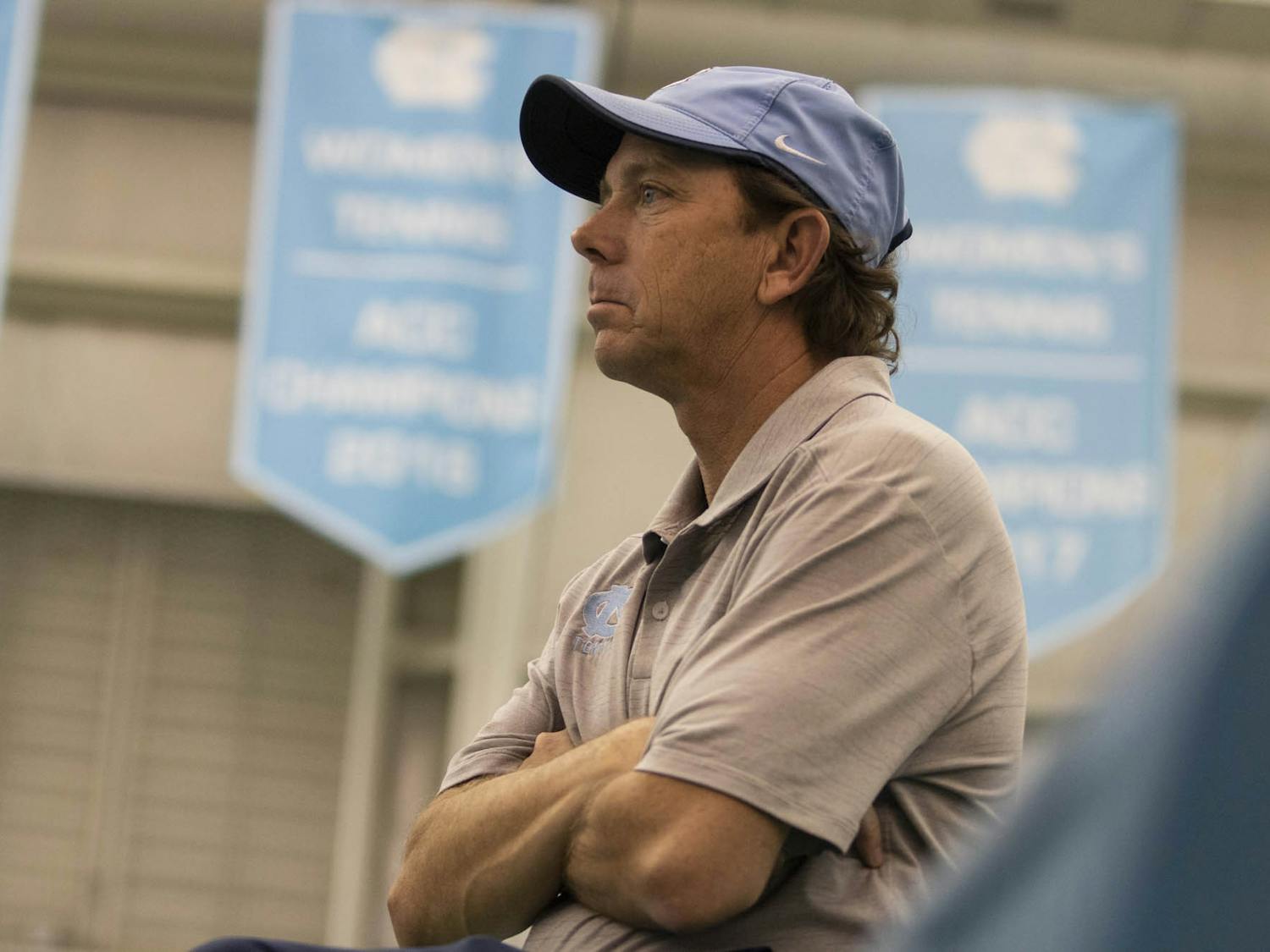 UNC women's tennis Head Coach Brian Kalbas crosses his arms on the sidelines as he observes the team play against Vanderbilt on Sunday, Feb. 2, 2020. UNC won 7-0.