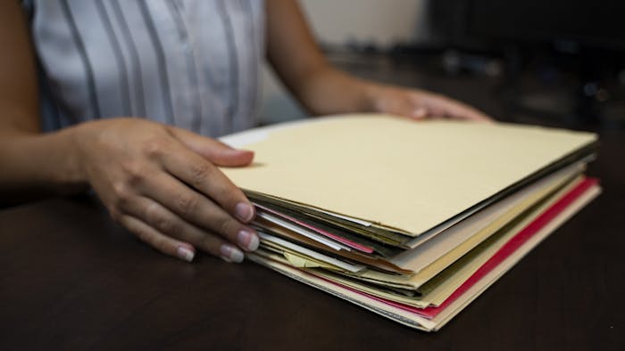 DTH Photo Illustration depicting a person handing over 15 file folders.