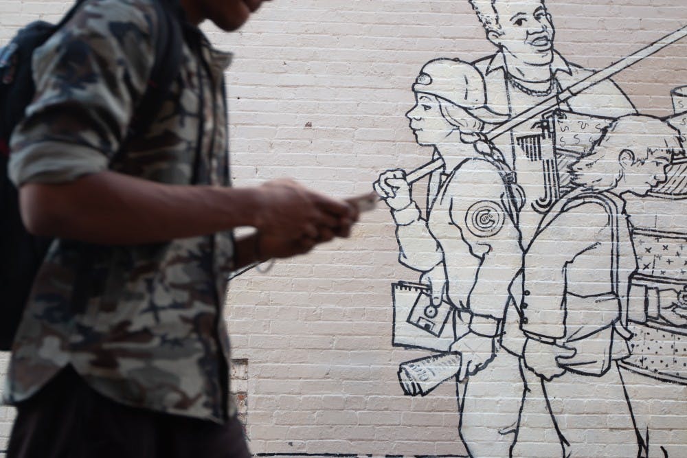 A student passes by a mural outside of Carolina Coffee Shop on Tuesday, Feb. 5, 2019. The mural, titled "Parade of Humanity" and created by Michael Brown, was restored in 2008 and stands as one of several pieces of public art in Chapel Hill. 