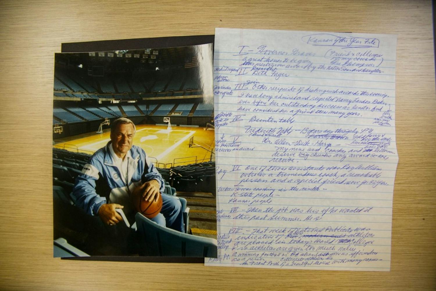 A photo of Dean Smith in the Dean Smith Center rests next to hand written notes Smith wrote in preparation for his speech in 2001 after being named Kansan of the Year.
