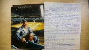 A photo of Dean Smith in the Dean Smith Center rests next to hand written notes Smith wrote in preparation for his speech in 2001 after being named Kansan of the Year.