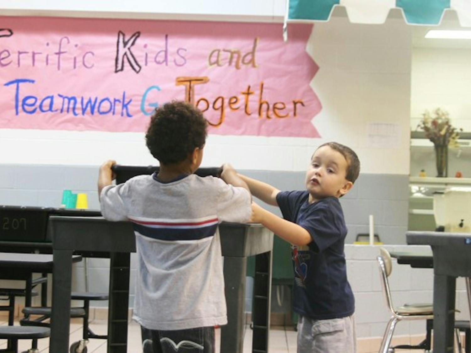 Five-year-olds Justin McCrae (left) and Cameron Morely (right) help each other carry their kindergarten class’ plastic tub back to the cafeteria after eating the day’s fruit snack.
