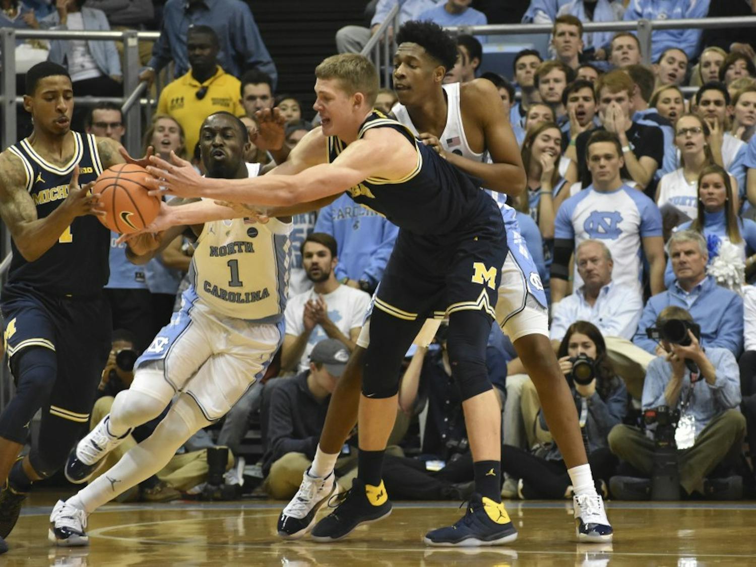 Theo Pinson (1) and Sterling Manley (21) reach to defend a Michigan handoff at the Dean Smith Center on Nov. 30.
