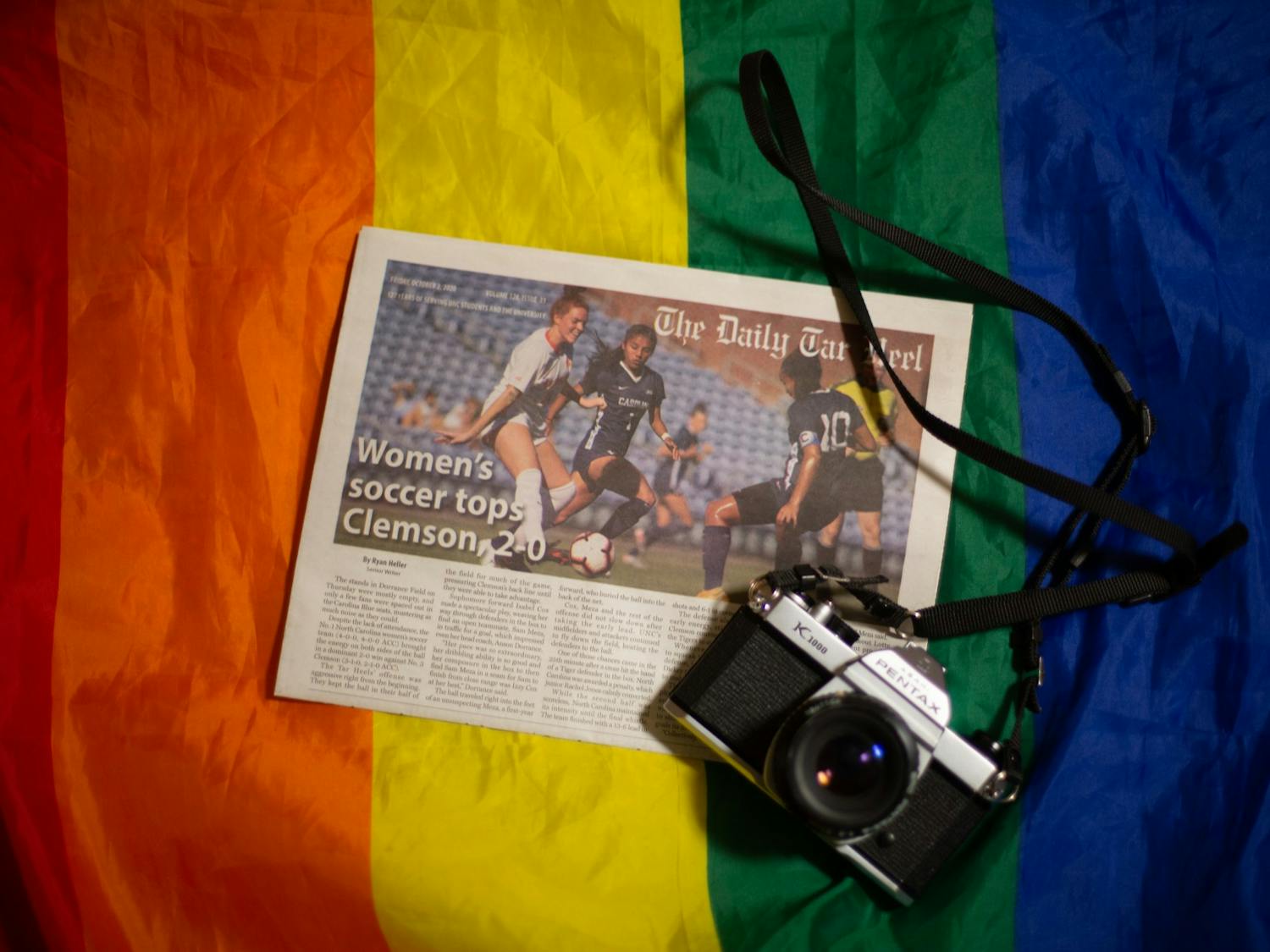DTH Photo Illustration. A copy of the Daily Tar Heel and a film camera sit on top of a rainbow pride flag.