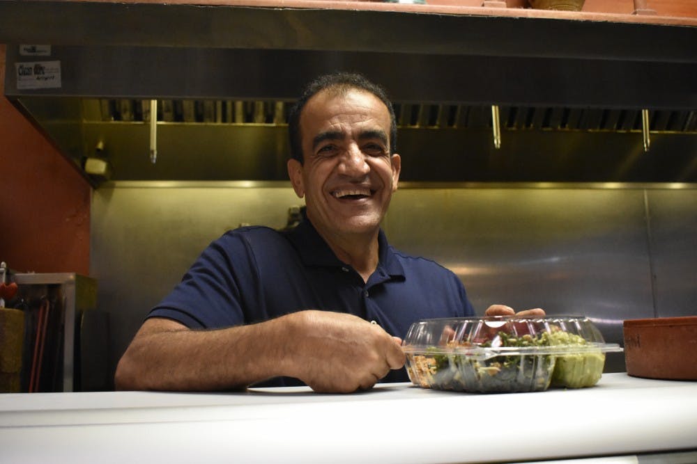 <p>Jamil Kadoura, owner of Mediterranean Deli, smiles as he finishes preparing a plate for a customer.&nbsp;</p>