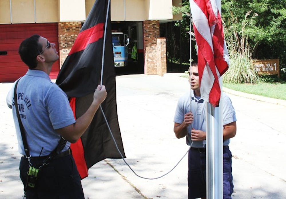 Chapel Hill fire department workers John Wellons (left) of Durham and Michael Crabtree (right) of Whitsett raise the fallen firefighters flag. 