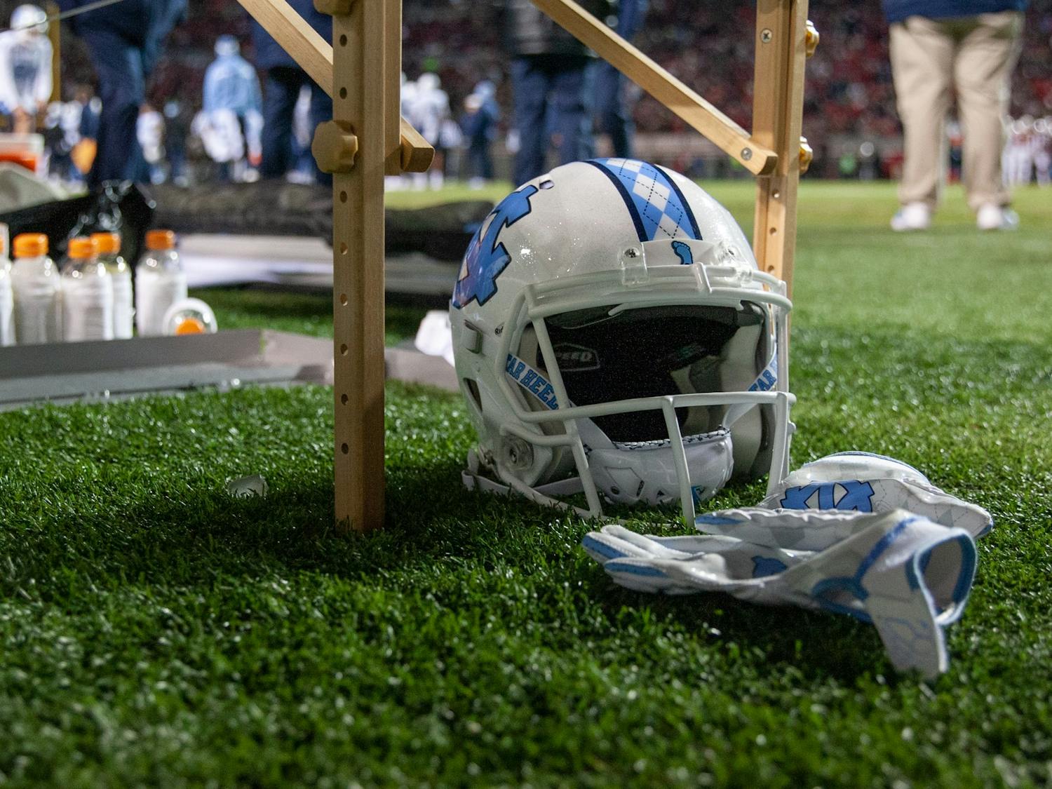 A UNC football helmet and gloves lie under a table during the Tar Heels' football game against the N.C. State Wolfpack at Carter Finley Stadium in Raleigh, NC, on Friday, Nov. 26, 2021. UNC lost 34-30.