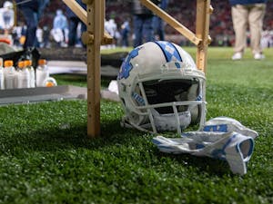 A UNC football helmet and gloves lie under a table during the Tar Heels' football game against the N.C. State Wolfpack at Carter Finley Stadium in Raleigh, NC, on Friday, Nov. 26, 2021. UNC lost 34-30.