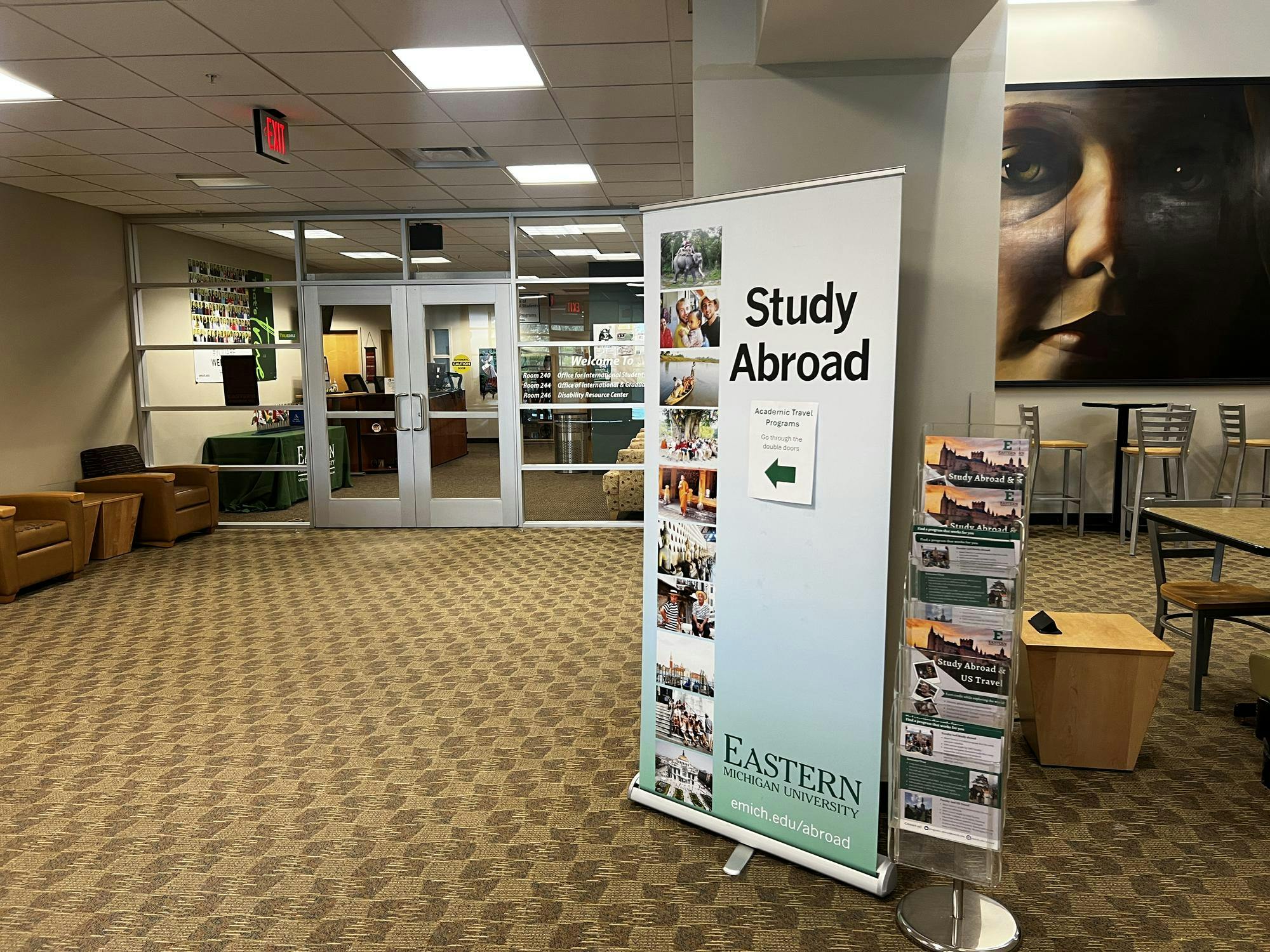 A photo outside of the Office of Academic Travel Programs. There is a tall banner pointing to the office doors that says "Study Abroad" and "Go through the double doors". 