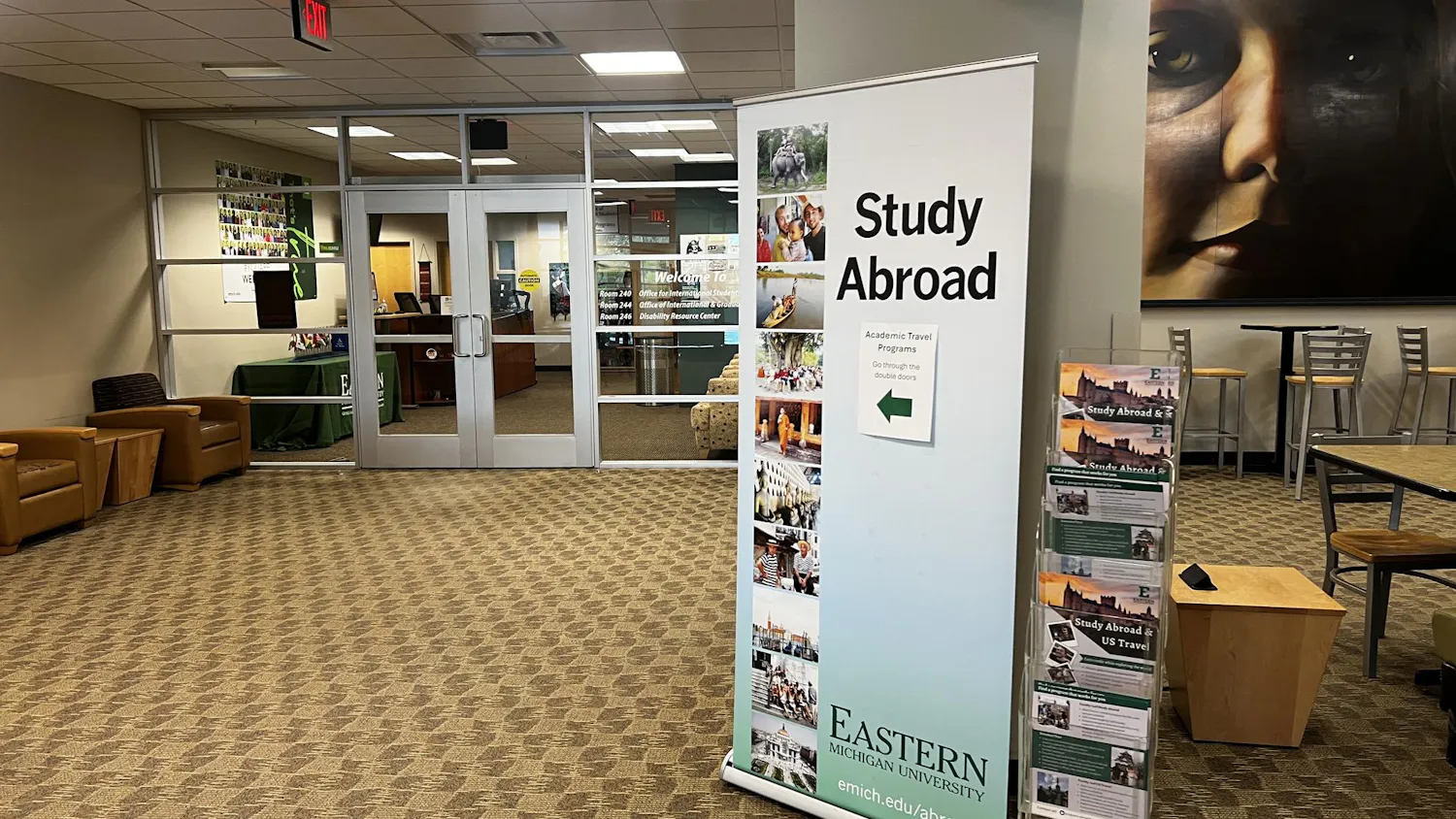 A photo outside of the Office of Academic Travel Programs. There is a tall banner pointing to the office doors that says "Study Abroad" and "Go through the double doors".