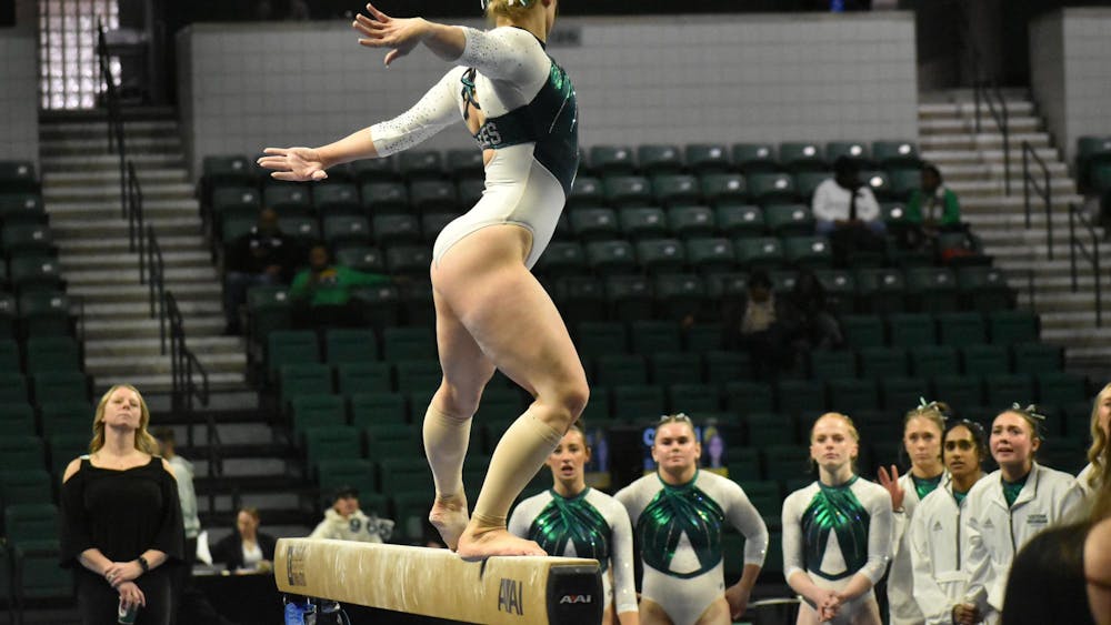 Gymnast Kyrie Lowe poses on the balance beam. Her team watches her in the background.