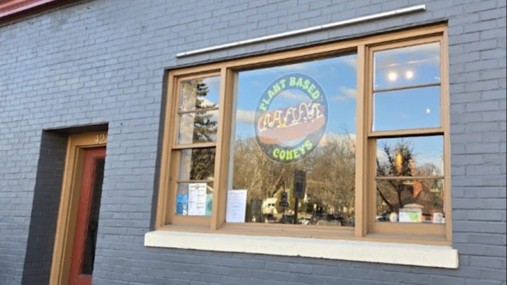 Gray brick exterior of Plant Based Coneys restaurant. Window with hot dog logo and "Plant Based Coneys" decal.