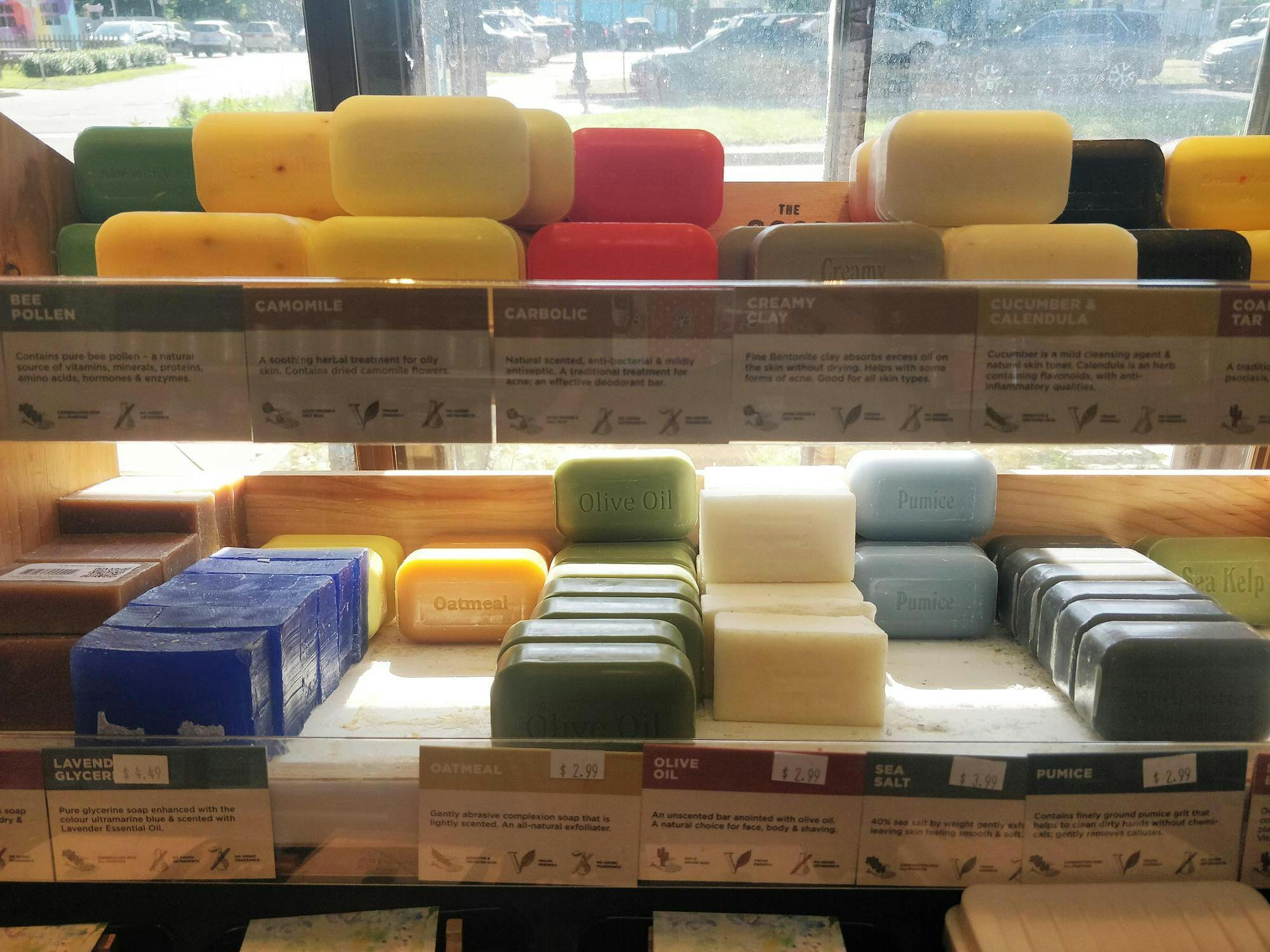 Natural bar soaps with no packaging line two shelves in rows, sorted by their color and scent. Scent names are carved into most of the soap bars, and tags in front of each type explain the ingredients used in each.