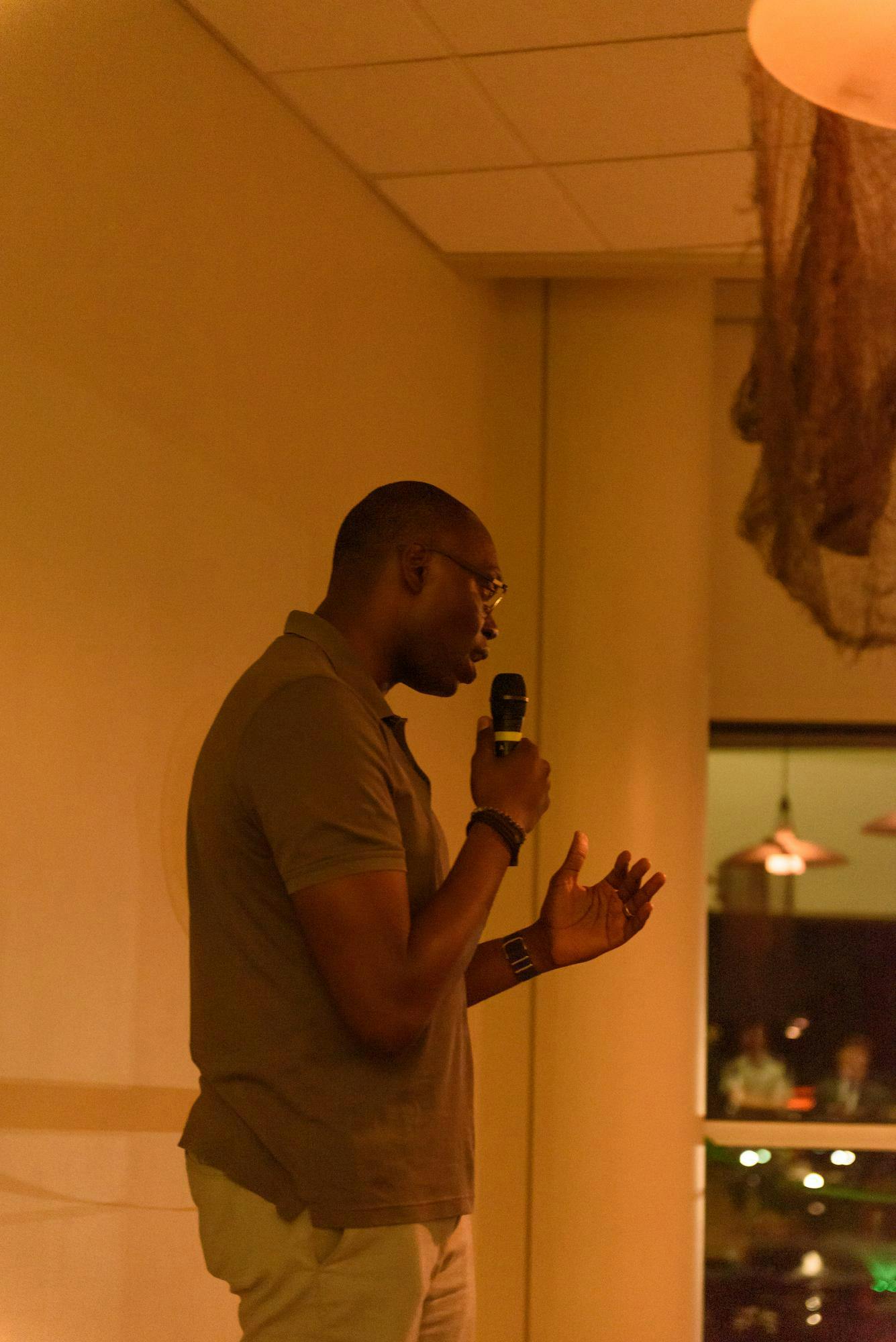 A person holds a microphone and looks to the crowd as they speak.