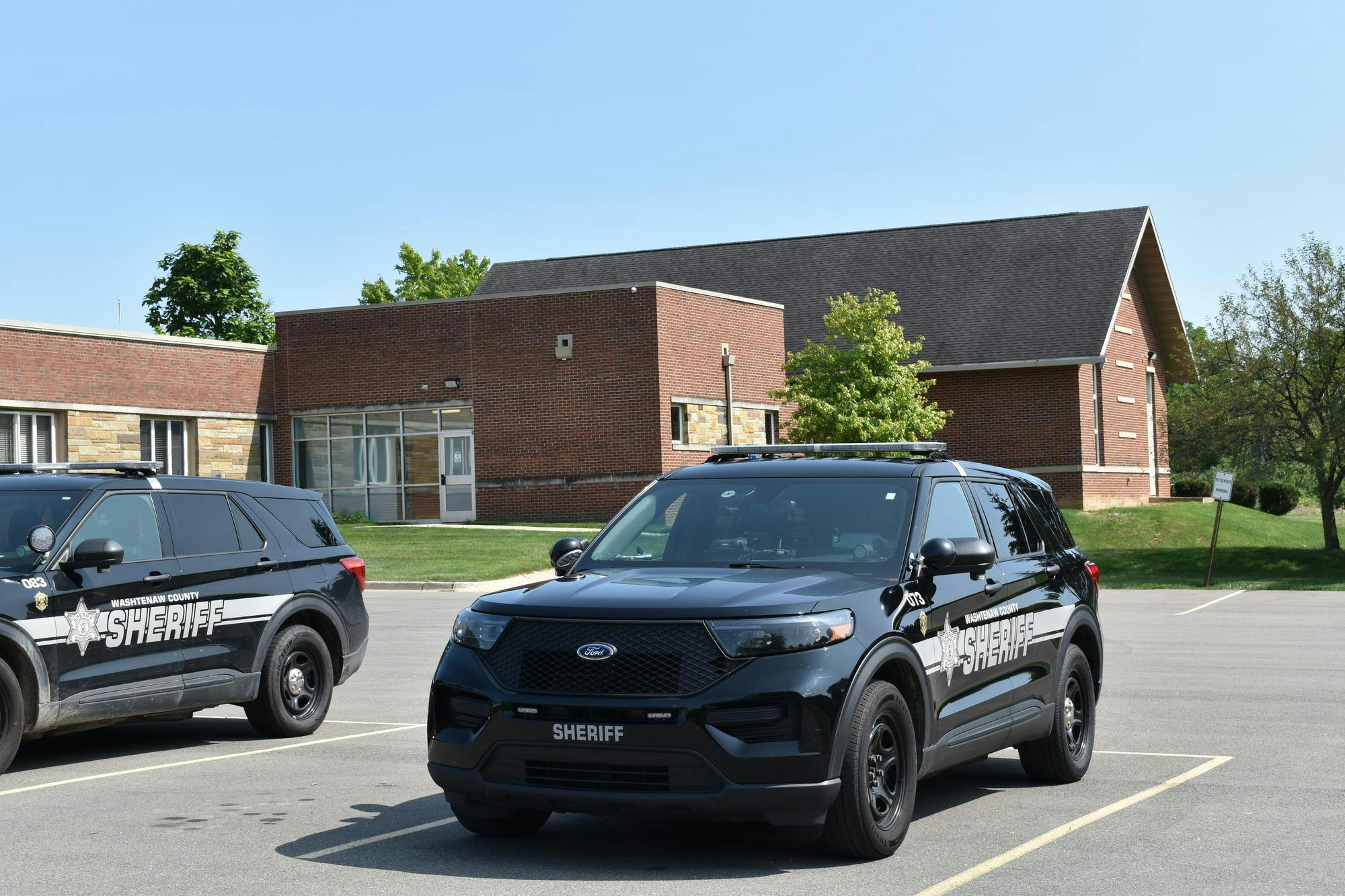 Two all black police cars are parked, with the sheriff office in view behind them.