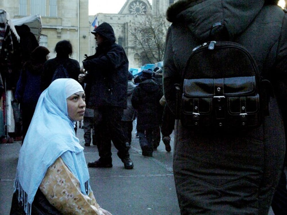 A young Muslim woman begs for money at an outdoor market in Saint-Denis, France.  In 2004, the French government imposed a law banning the public display of religion, including the hijab, in schools.