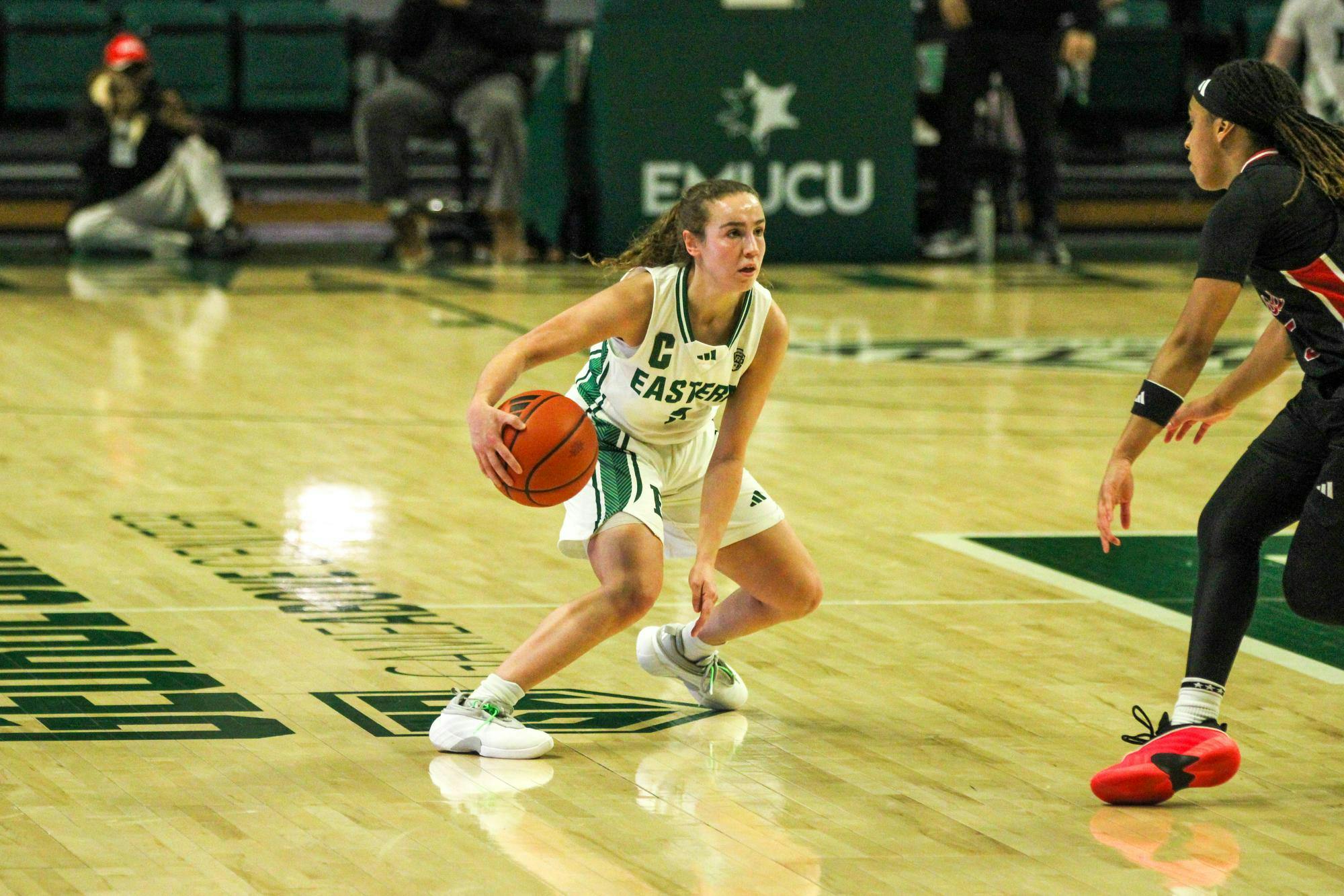 EMU player #7, in a white jersey, dribbling the basketball.