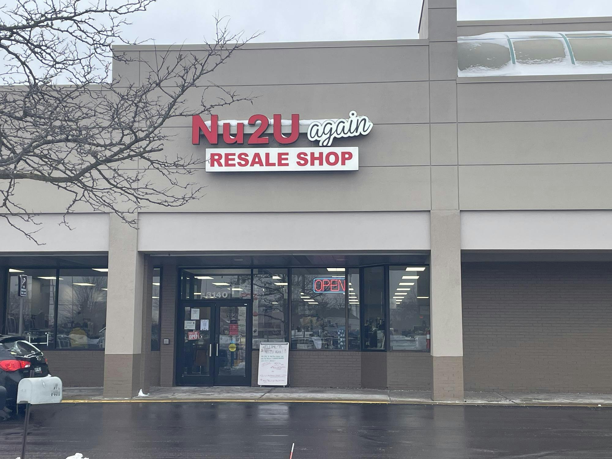 A brown building with a signboard outfront, an open sign in the window and the name displayed at the top of the building, Nu2U Again Resale Shop.