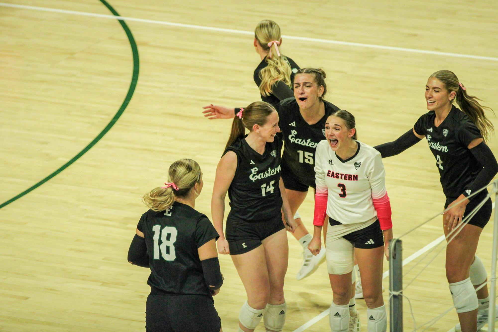 EMU players in black jerseys, and one in a white jersey, celebrating after getting a point. 