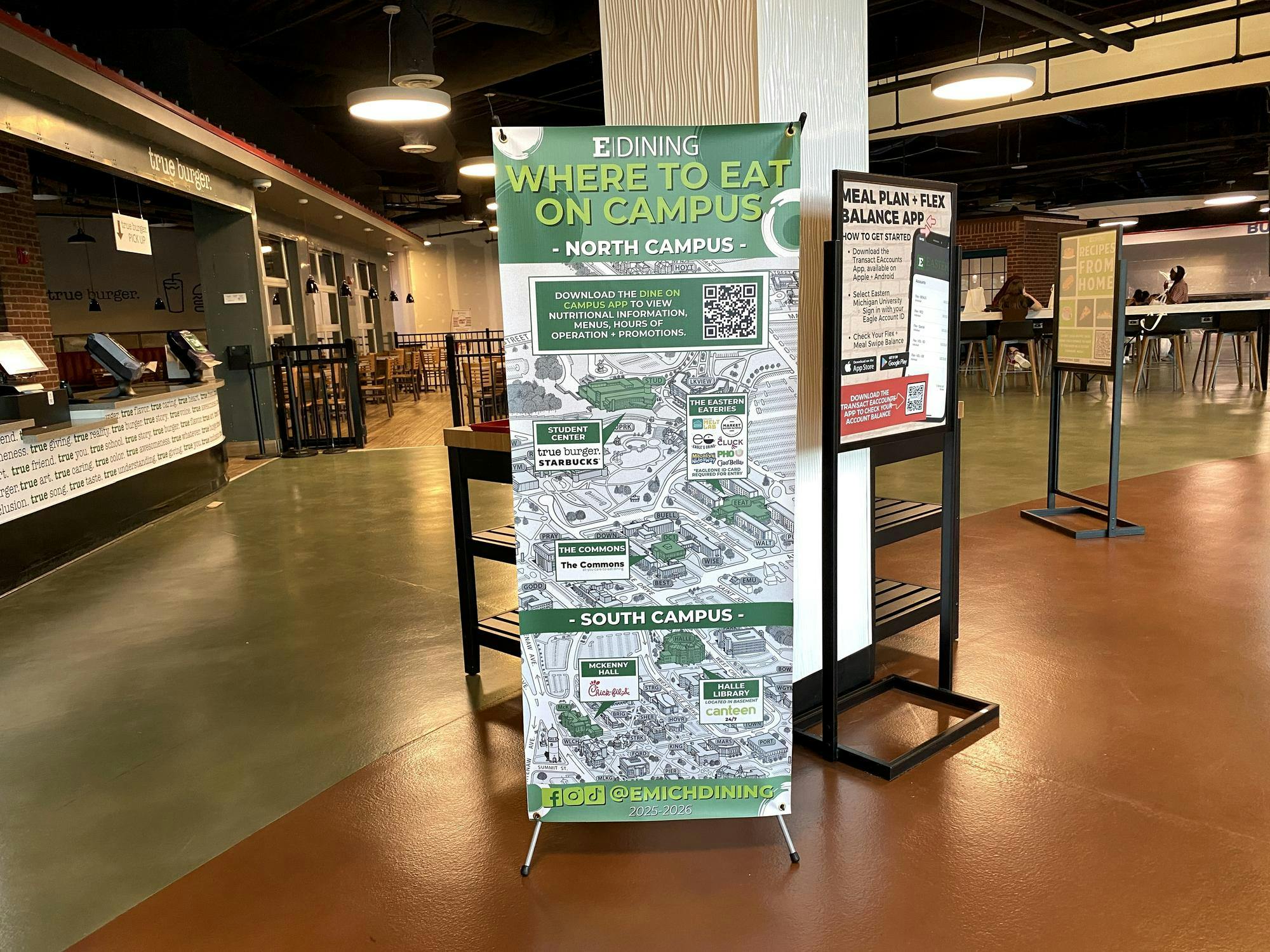 The green, white, and gray sign has an EMU map in the background with the different dining locations identified in smaller graphics throughout the sign.