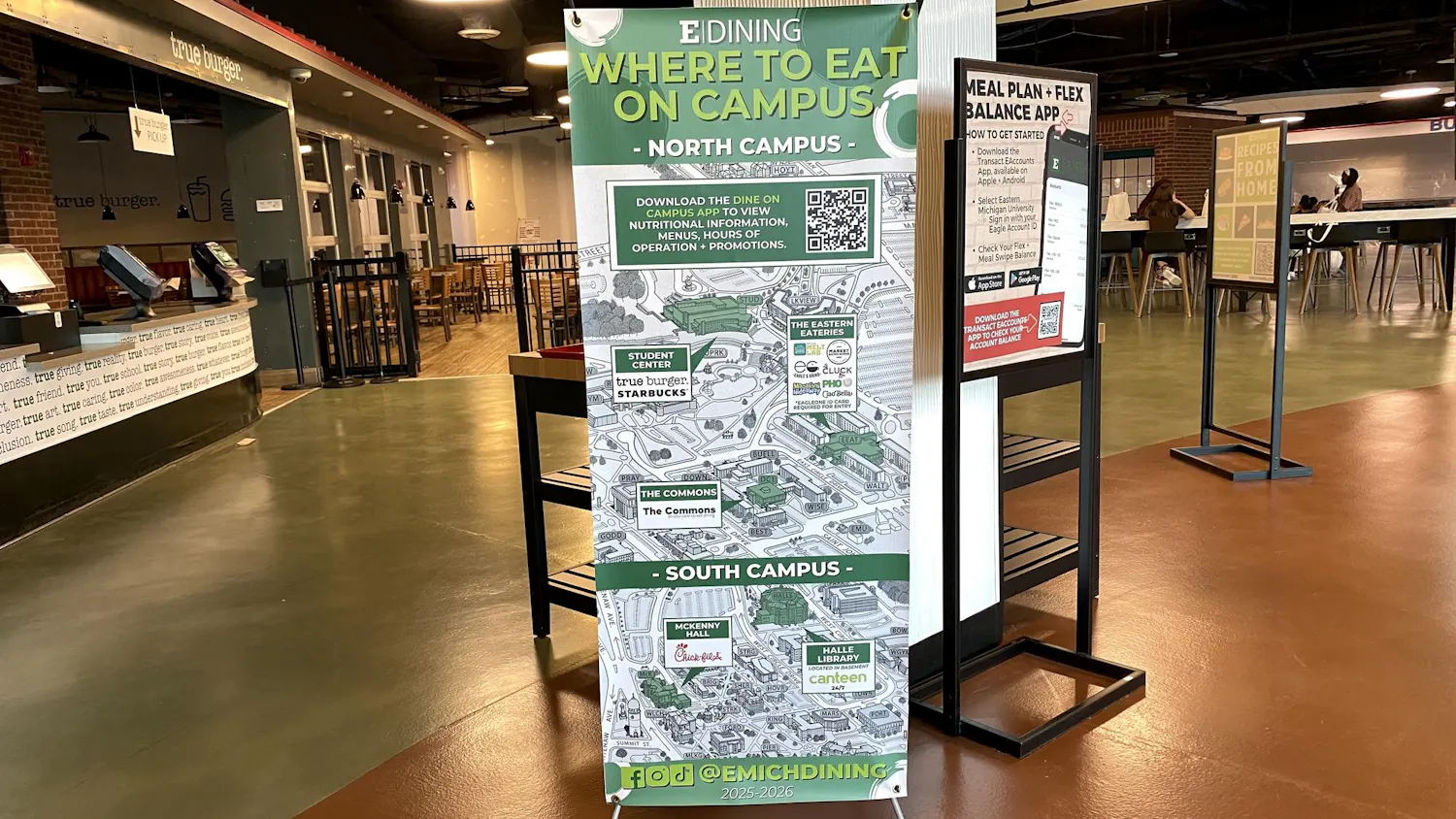 The green, white, and gray sign has an EMU map in the background with the different dining locations identified in smaller graphics throughout the sign.