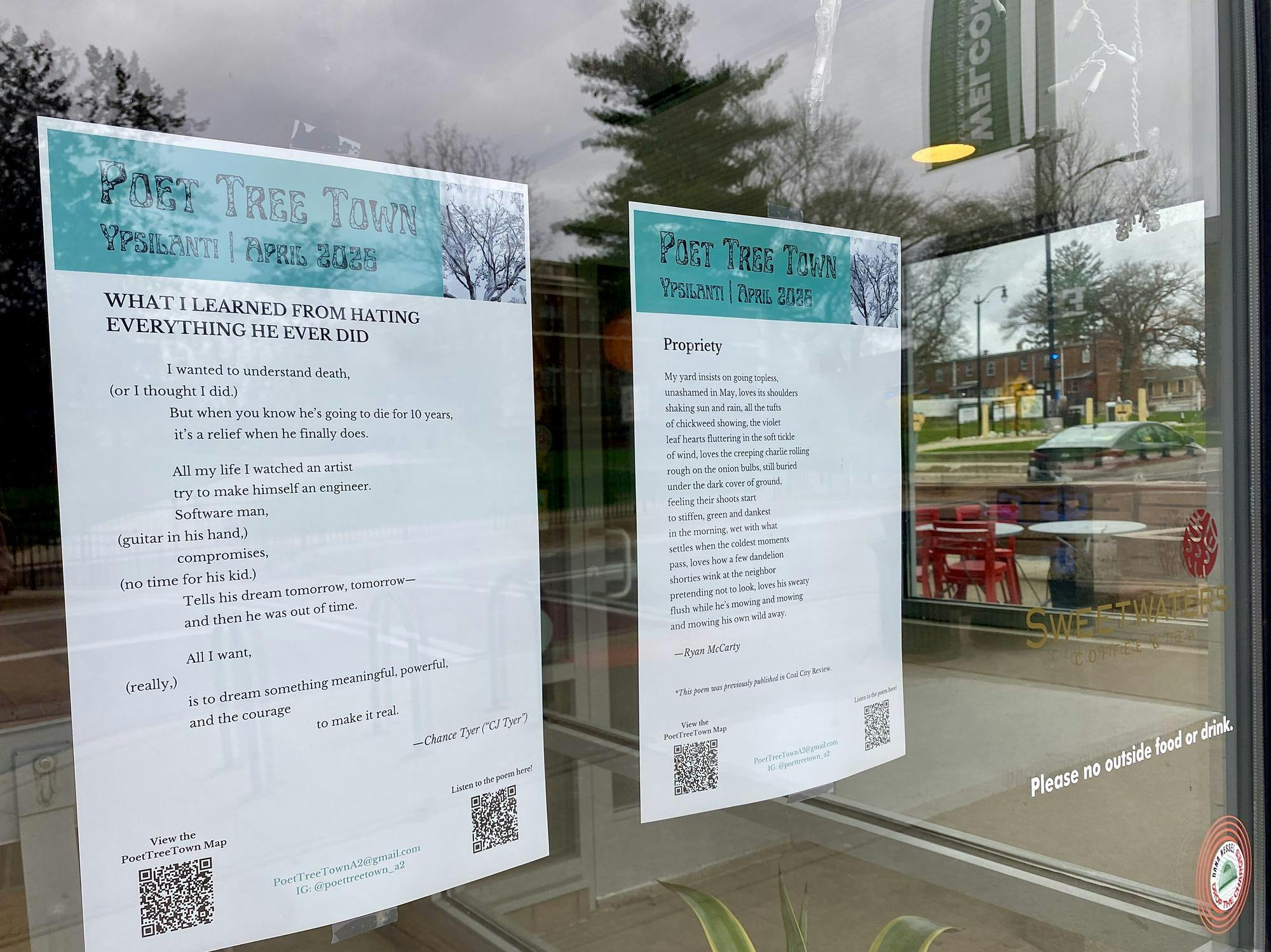 Two pieces of paper featuring poems are taped to the inside of a storefront window. A parking lot can be seen in the background through the window.
