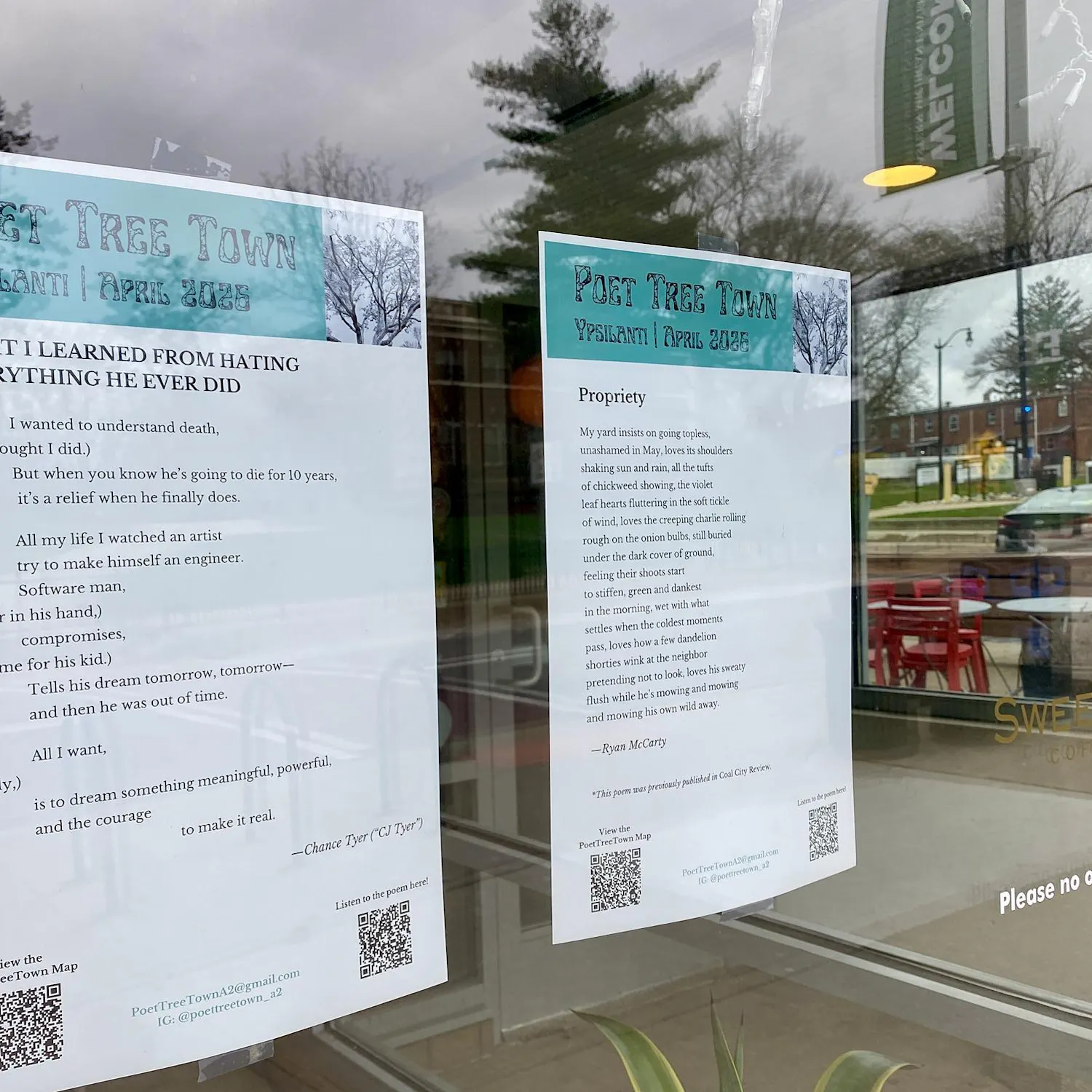 Two pieces of paper featuring poems are taped to the inside of a storefront window. A parking lot can be seen in the background through the window.