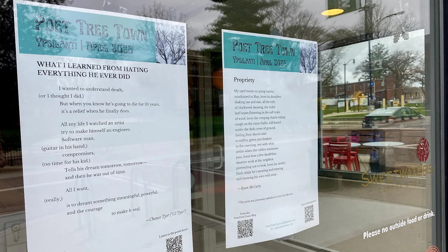 Two pieces of paper featuring poems are taped to the inside of a storefront window. A parking lot can be seen in the background through the window.