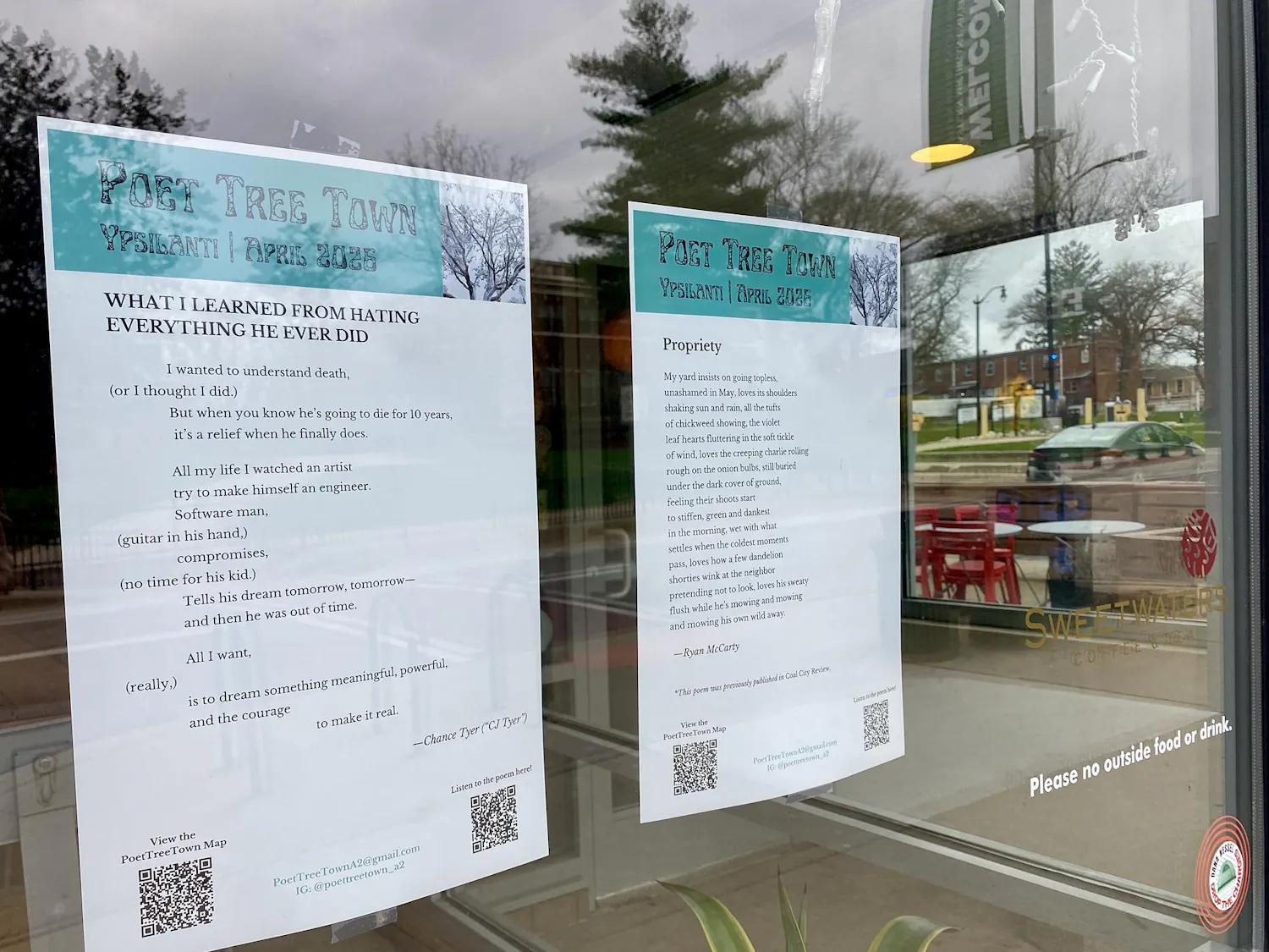 Two pieces of paper featuring poems are taped to the inside of a storefront window. A parking lot can be seen in the background through the window.
