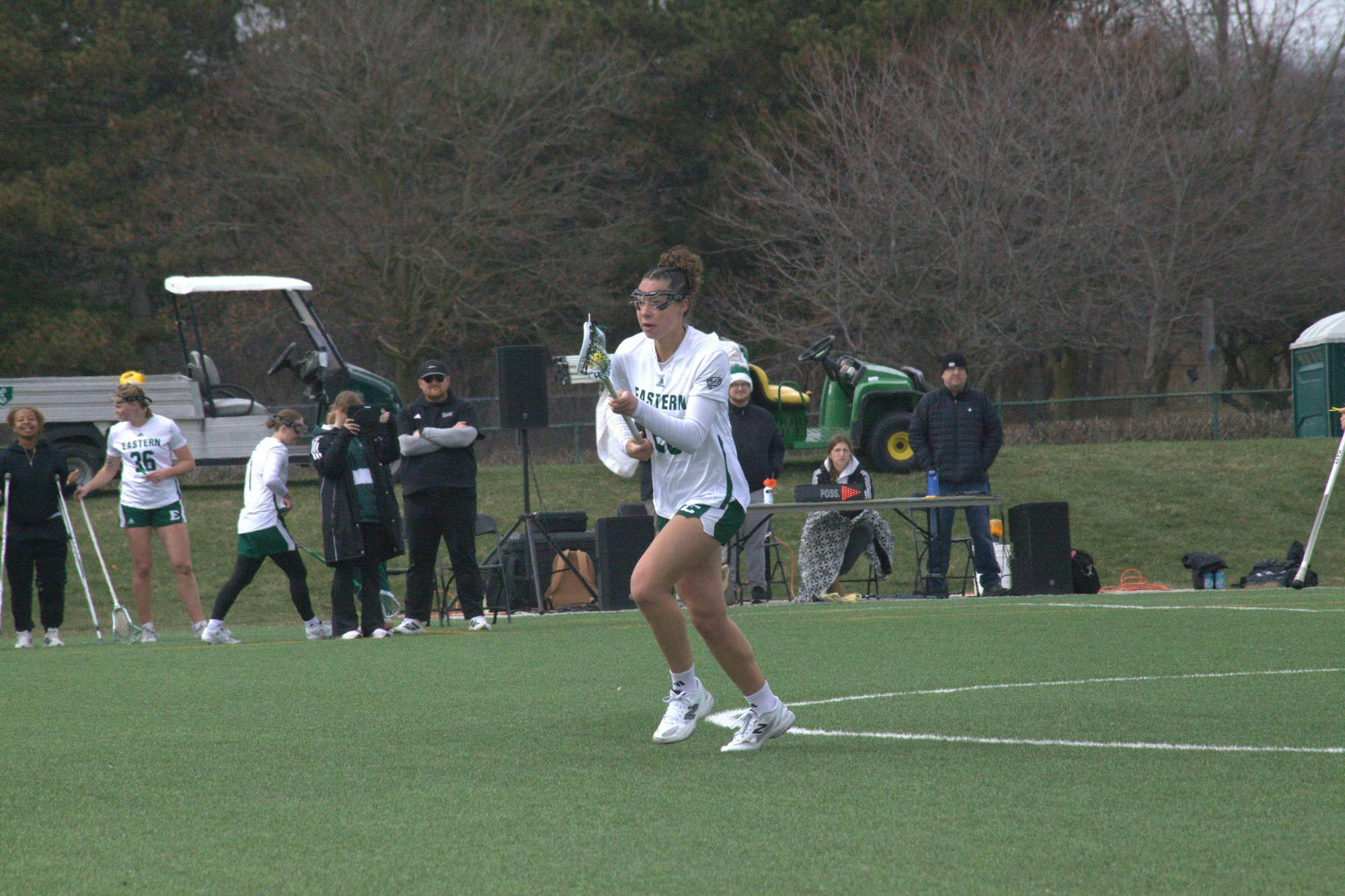 Women's lacrosse player cradles the ball mid-step on outdoor lacrosse field.