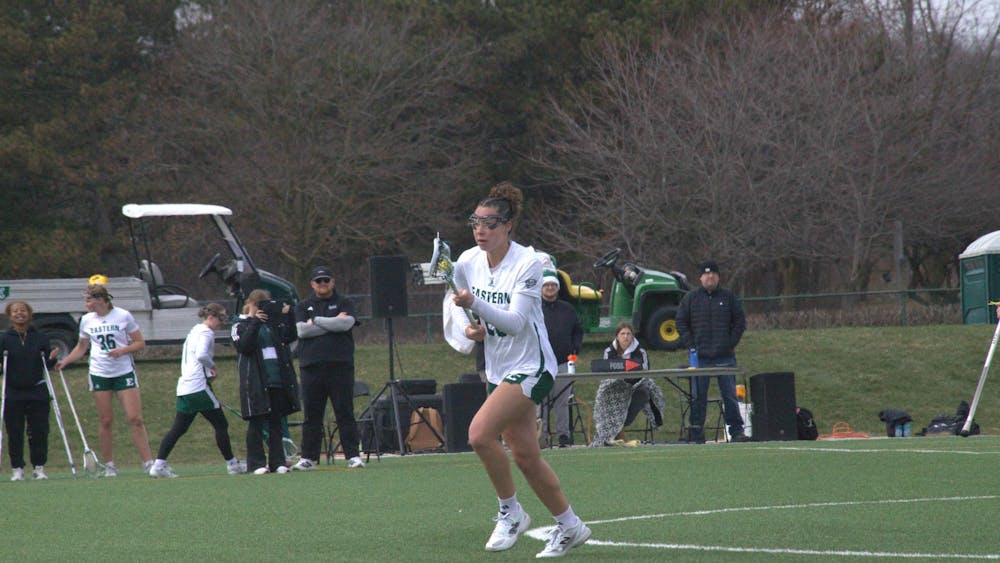 Women's lacrosse player cradles the ball mid-step on outdoor lacrosse field.