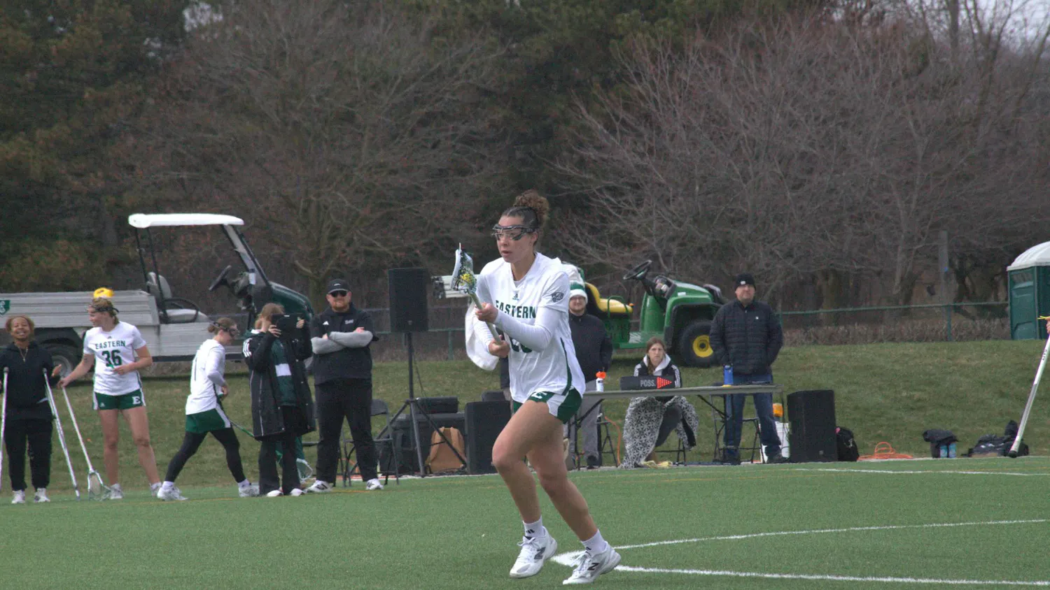 Women's lacrosse player cradles the ball mid-step on outdoor lacrosse field.