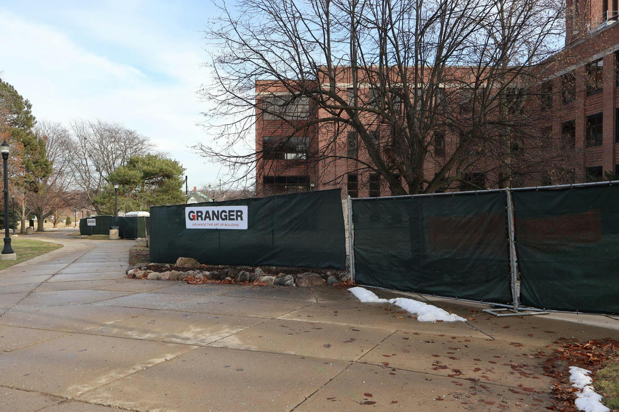 Green construction fences outside Pierce Hall line the campus sidewalks and block the view of the construction happening behind them.