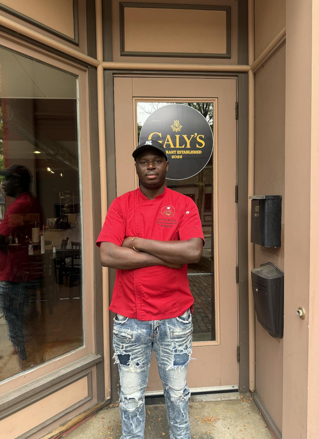 A man in a red chef's coat stands in front of his restaurant.