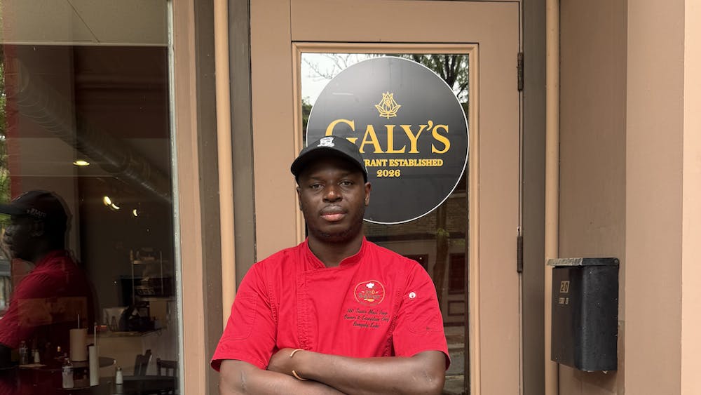 A man in a red chef's coat stands in front of his restaurant.