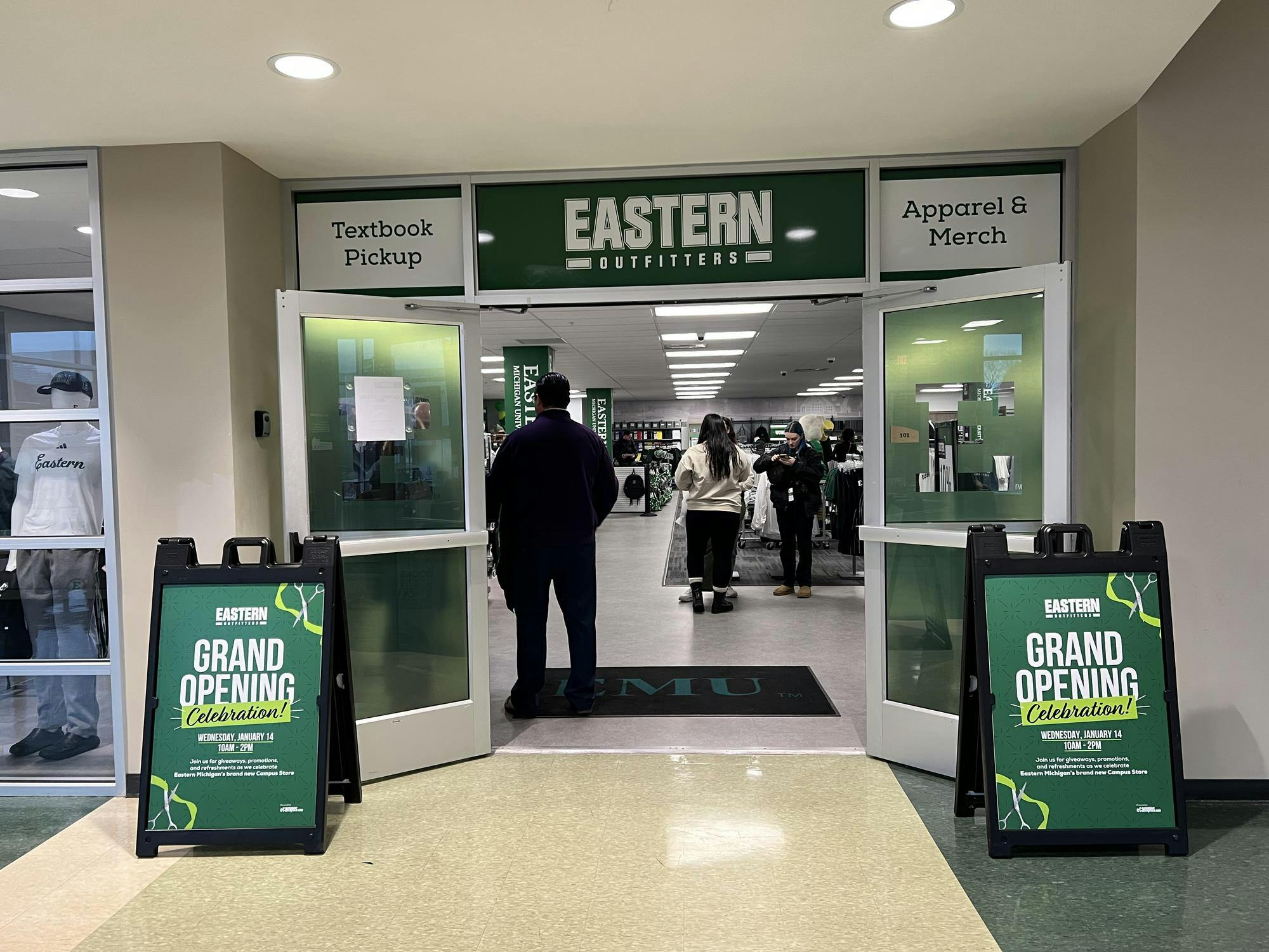 A storefront with its double doors propped open labeled with a banner that says "Eastern Outfitters," alongside two signs that say "Grand opening celebration!" 