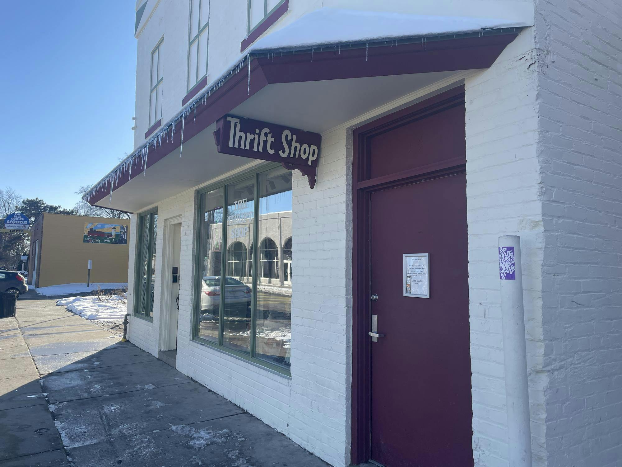 A white brick building with a sign that says "Thrift Shop" coming from the building and icicles hanging off of the building awning.