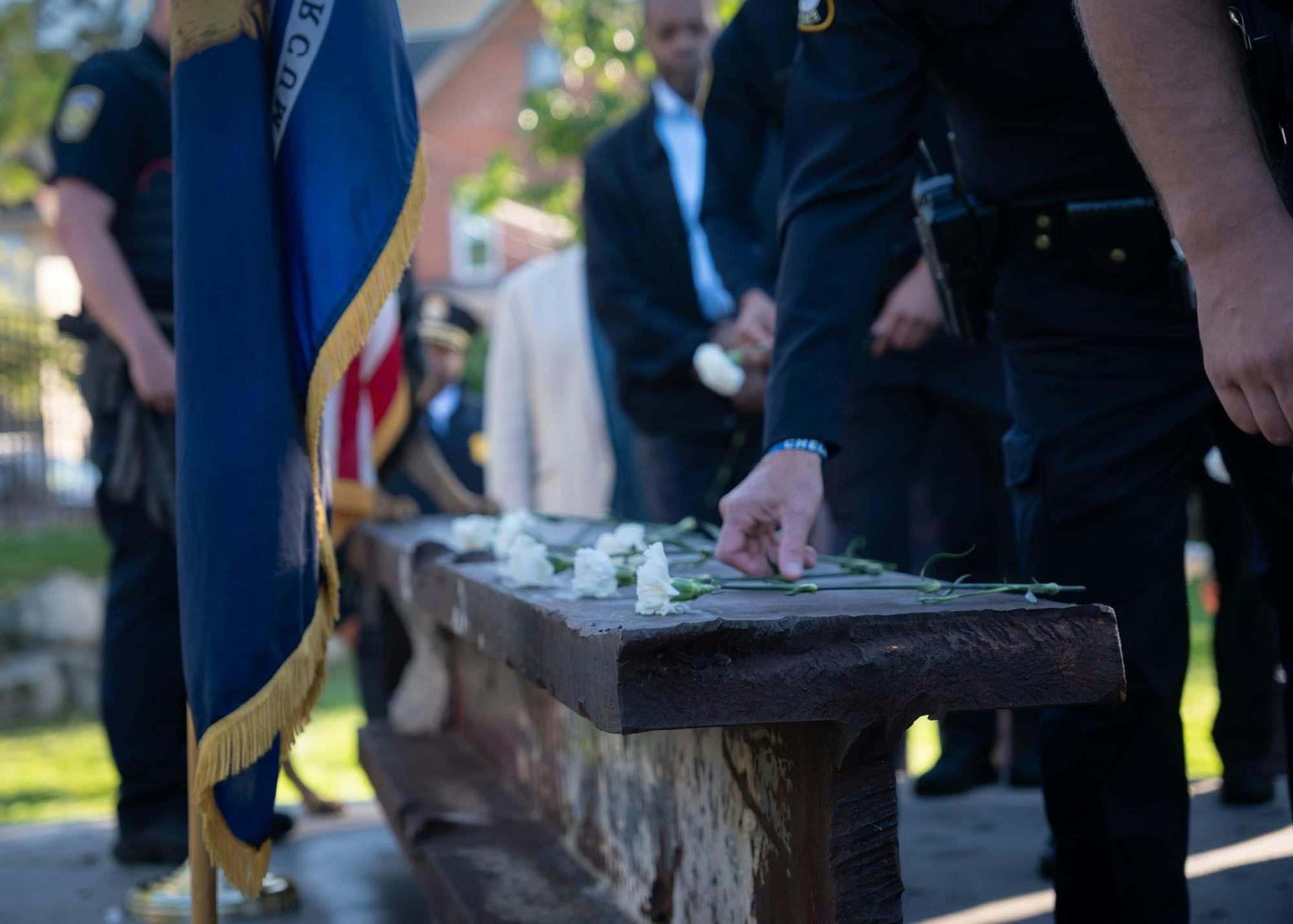 White carnations are seen placed on top of the recovered steel beam from the South Tower of the World Trade Center, part of the EMU campus 9/11 memorial. Waist down, a line of people in uniforms line up to place the flowers.