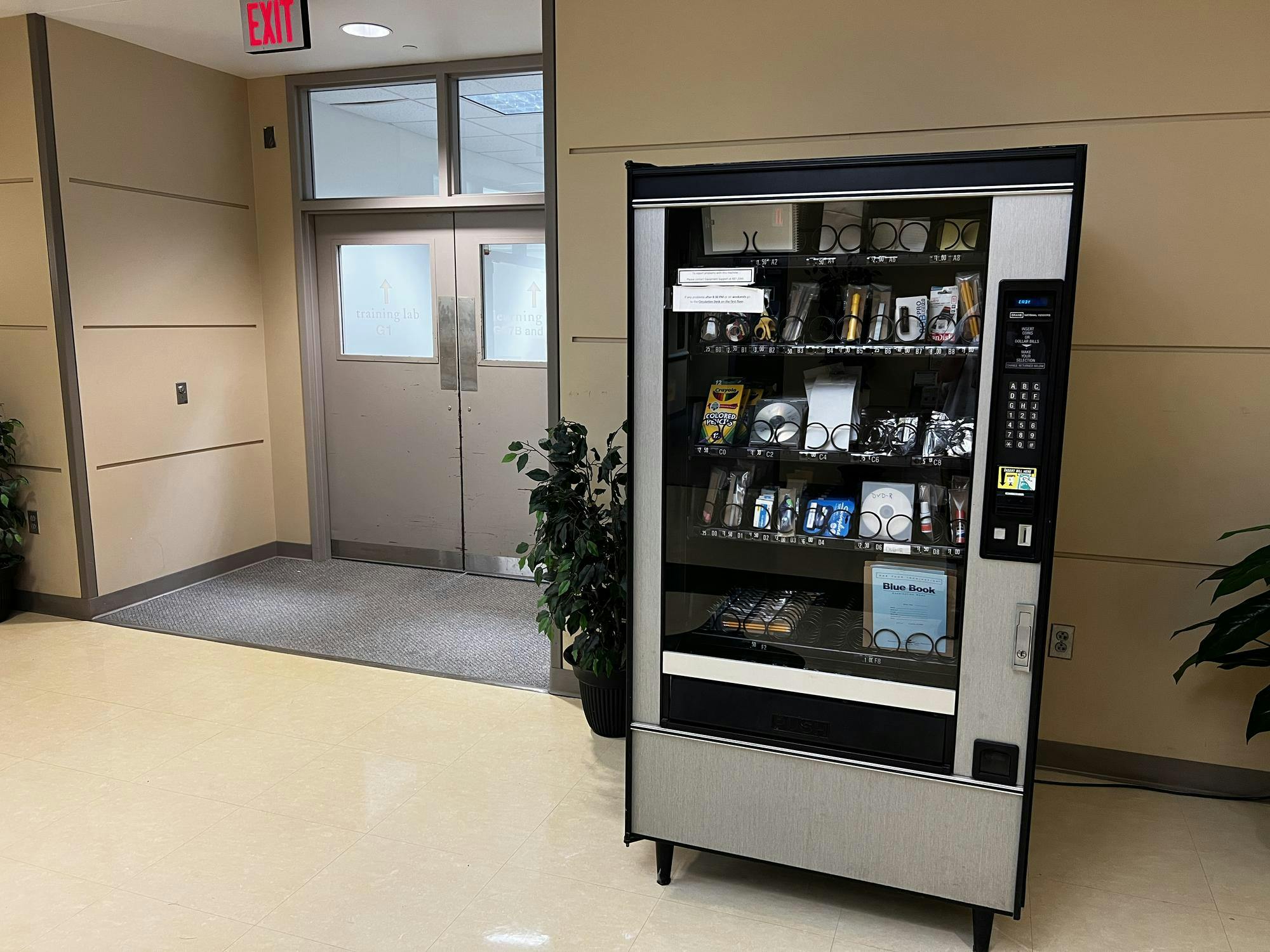 A large silver and black vending machine that contains stationery items and basic tech items, such as SD cards and CDs.